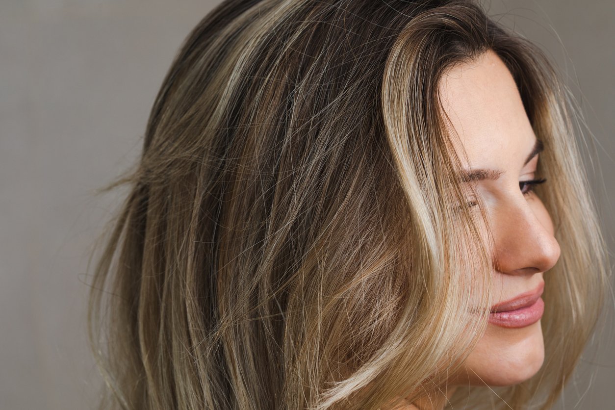 Closeup einer lächelnden, jungen, blonden Frau mit glatten, gefärbten Haaren, die zur Seite schaut